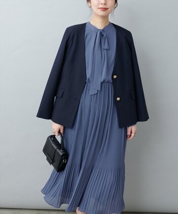 細かなプリーツが女性らしいボウタイワンピースは、ややグレーがかったブルーが上品。首元でリボン風に結えば、アクセサリーがなくても華やかな印象に。ダークカラーのジャケットでコーデを引き締めたところも巧みです。
