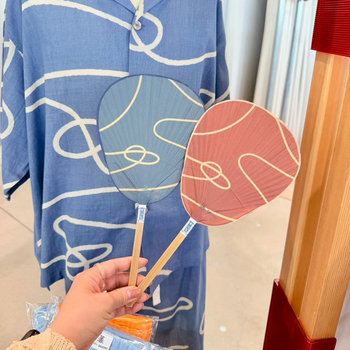 「栗川商店」別注“ゆ”うちわ。来民渋うちわをベースに、ウェアとおそろいの3色＋監修カラーを含む全5色展開。ここでしか手に入らない万博限定カラー（写真右）に惹かれて、スタッフも思わず購入。