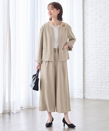 前身頃のみに裏地を施すことで肩まわりの窮屈感を解消した軽やかなベージュカラースーツ。淡い色味は、写真撮影の際の顔写りを明るく見せてくれる効果も期待できます。
ゆったりシルエットのノーカラージャケットと、タック入りでドレープが美しいワイドボトムの組み合わせは、パンツスタイルながら女性らしい印象に。