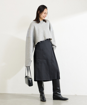 ぺたんこの黒ロングブーツは、足元だけに重心が行きがち。同じ黒のスカートを合わせてブーツと繋げることで、スラリと脚長のラインを演出できます。ショート丈トップスを合わせると、胴＜脚の比率になって、より効果的です。