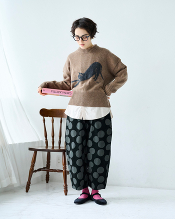伸びをする猫が描かれた目を引くニットに、ドットのコーデュロイパンツを合わせた、チャーミングな組み合わせ。印象的な柄同士でも、落ち着いたトーンに揃えることで大人っぽく仕上がります。ニットの前身頃は短めなので、シャツをレイヤードして抜け感をプラスして。
