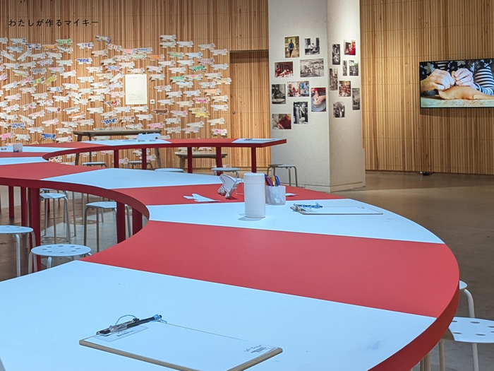 大きな楕円状の空間で展開するワークショップ。中央には、赤と白の縞模様が特徴的な猫のマイキーを連想させるテーブルが置かれ、自由にお絵描きを楽しめます