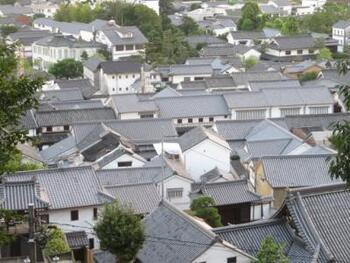 “本町通り”・東町エリアは、小高い鶴形山（つるがたやま）の南方裾野に弧を描くように形成された、倉敷の発祥の地。江戸初期に新田開発で広がった集落が、物資の集散地として栄えるにしたがって、商家や庄屋、職人らの家々が建ち並び、現在の町の原型を形成しました。【画像は江戸から明治の面影を残す、町家や蔵が連なる“本町通り”。】